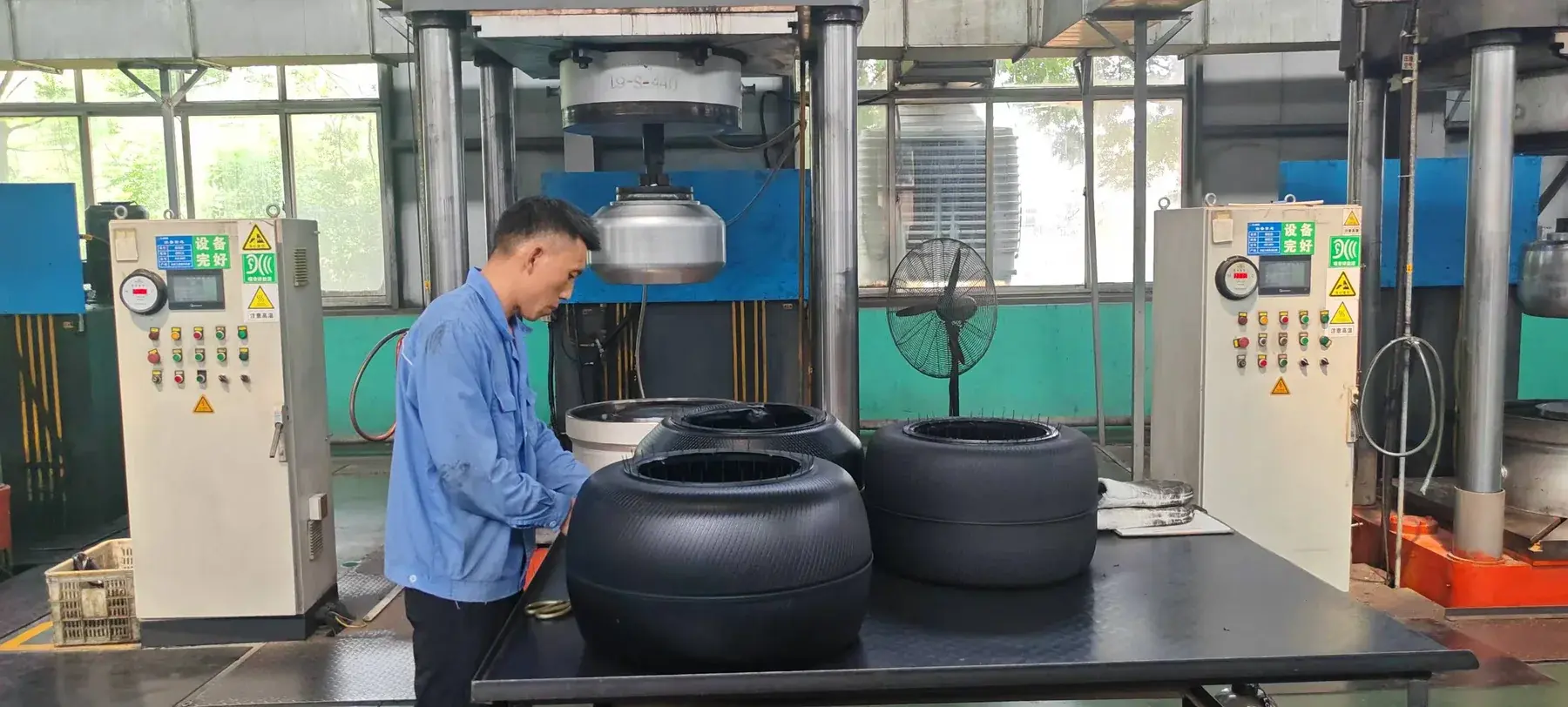 Worker handling tire curing bladders at a molding workstation in a manufacturing supply facility